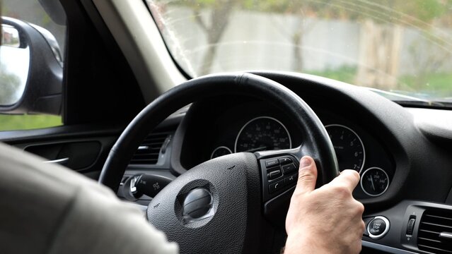 Male arms holds steering wheel while driving a motor car at city. Young man riding on electric automobile at urban road. Driver moving on his electrical auto on route. Slow motion