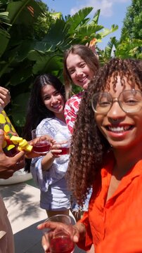Group of happy multiracial friends dancing, eating watermelon and pizza, and drinking at an outdoor party on a sunny day, with one woman recording a selfie video of the joyful moment