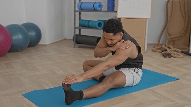 Man stretching leg on blue yoga mat in studio reaching for foot and holding knee; determination recovery.