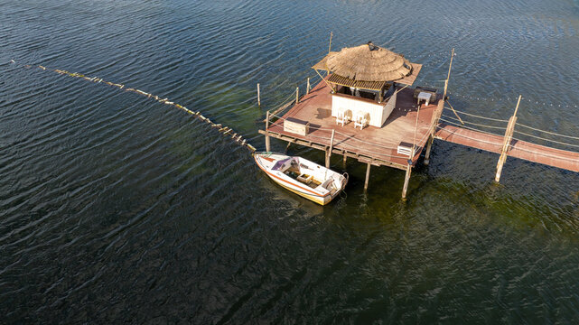 Aerial view of a traditional thatched roof hut on stilts with a small boat moored alongside at Salinas de Aveiro, Aveiro, Portugal.