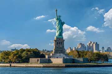 Close-up view of the Statue of Liberty with NYC skyline under a clear blue sky. © VisualCoordinates