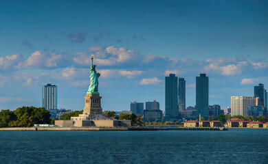 Statue of Liberty with Manhattan skyline under blue sky and clouds, iconic New York landmark view. © VisualCoordinates