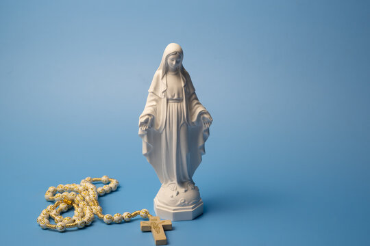 Virgin Mary statue with rosary and cross on blue background, studio shot, selective focus with copy space