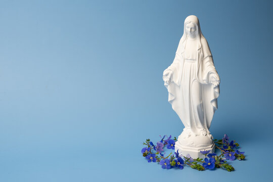 Virgin Mary statue with blue flowers on blue background, studio shot, selective focus with copy space