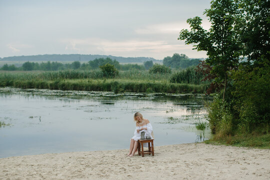 Woman sculpting clay by river wetlands at sunrise