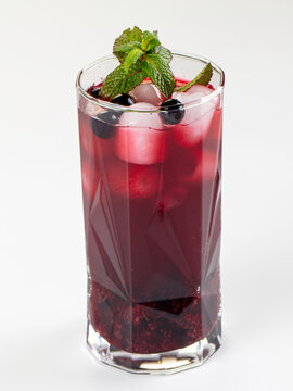 Refreshing berry cocktail with mint and ice in a faceted glass, isolated on a white background.