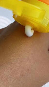 White skin cream coming out from yellow bottle packaging onto hand skin. Close up view, moisturizing texture for daily skincare.