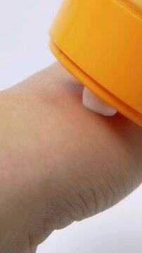 Pouring white cream from orange beauty product onto hand skin. Close up skincare concept in vertical view.