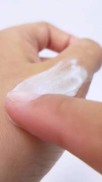 Applying white cream on hand skin. Vertical close up view on white background. Moisturizing skincare for soft healthy hands.