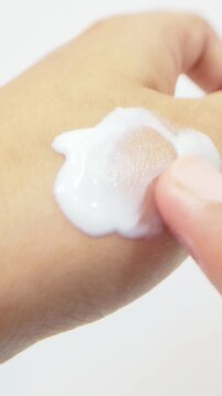 Applying soft white cream slowly to back of hand. Gentle moisturizing texture, daily skincare routine for smooth healthy skin.