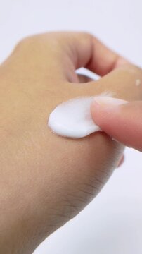 Gently applying white beauty cream on back of hand. Close up skincare concept on white background in vertical view.