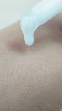 Pouring milky white serum onto hand skin using beauty serum pipette. Close up view. Moisturizing skincare treatment.