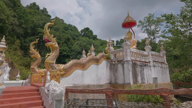 The Naga staircase and the Buddha statue are situated on a high point, offering a view of the mountains in the background. This is in the Lanna Thai style, Chiang Mai.