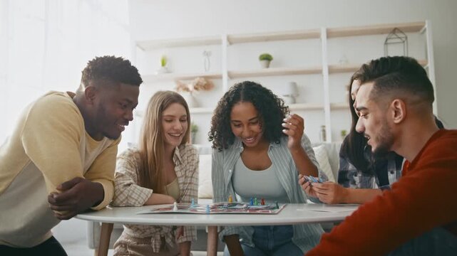 A group of four friends gather around a table for game night. They are engaged in playing board games, sharing smiles, and having a good time together. The room is well-lit, with a cozy atmosphere.
