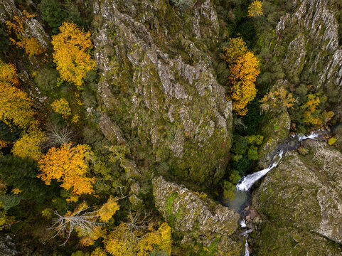 Aerial view of Poco do Inferno waterfall cascading through a rocky gorge surrounded by vibrant autumn foliage in Manteigas, Guarda District, Portugal.