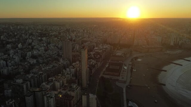 Drone aerial footage of golden hour sunset over Col&oacute;n Avenue and the coastline of Mar del Plata, Argentina, with Torre&oacute;n del Monje and Atlantic Ocean during winter. Urban coastal cityscape in South Am