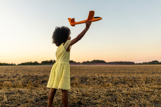 Pretty young african girl playing with airplane toy in the nature, concepts about sustainable lifestyle, green mobility and alternative transportation
