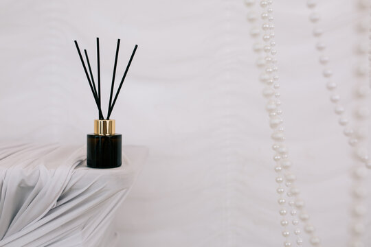An aromatic diffuser is located on a wooden fireplace, which is decorated with a white cloth. A glass bottle with essential oil containing reed sticks. Elimination of unpleasant odors