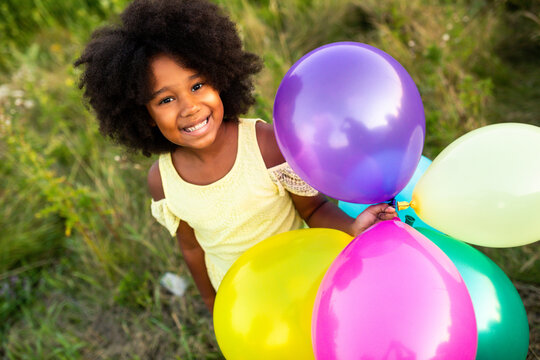 Pretty young african girl in a sunflowers field in bloom  playing with air balloons for her birthday party