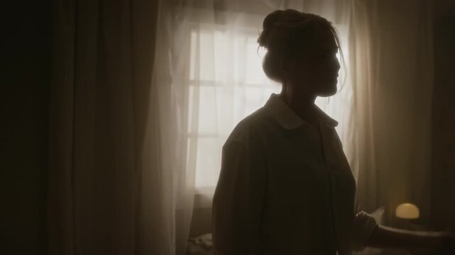 Medium handleld lowkey shot of young girl in white shirt with bun on head moving to music in sunlit morning bedroom