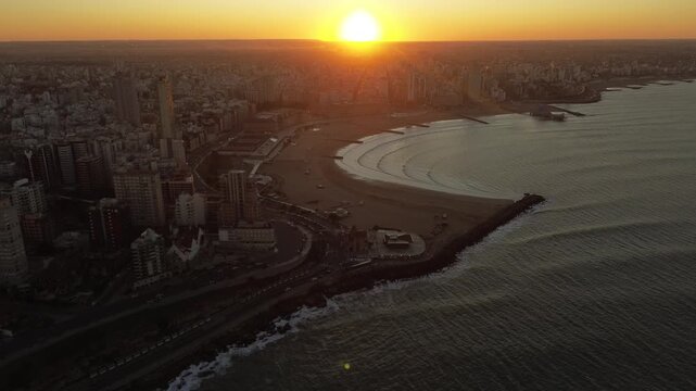 Drone aerial footage of golden hour sunset over Col&oacute;n Avenue and the coastline of Mar del Plata, Argentina, with Torre&oacute;n del Monje and Atlantic Ocean during winter. Urban coastal cityscape in South Am