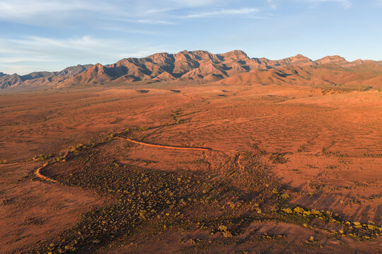Aerial view of the rugged mountain peaks and red desert landscape of the outback under a soft golden light in Flinders Ranges, South Australia, Australia.