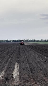 
Red Tractor Cultivating Agricultural Field at Dramatic Sunset. Red tractor cultivating and furrowing large dark soil agricultural field at dramatic cloudy sunset. Spring soil preparation and crop cul