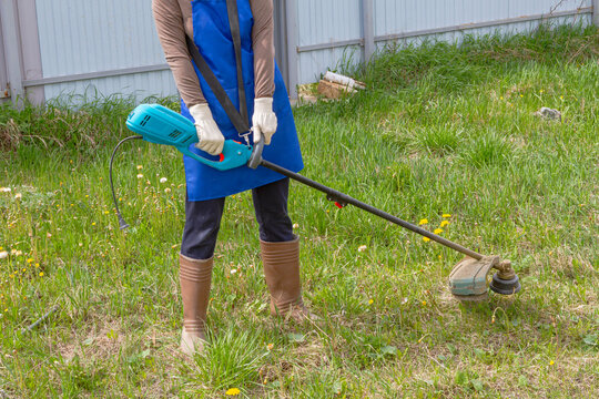 Woman gardener using electric corded string trimmer for grass mowing. Cable limitation during lawn care. Frustration with power wire and restricted movement when trimming garden weed