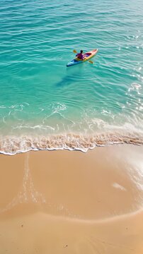 Kayaker paddling through turquoise ocean water near tropical sandy beach. High angle view with horizontal panning movement.