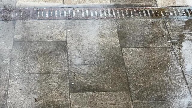 Path of stone tiles with metal storm drain during rain