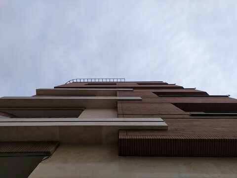 Modern multi story building corner with brown and beige facade against overcast grey sky. Architectural details and rooftop elements visible creating urban cityscape atmosphere in daylight.