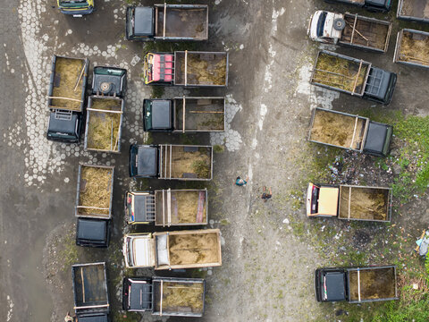 Aerial view of the Animal Market Prambanan with small trucks filled with hay parked in a lot and people walking between them in Kecamatan Prambanan, Jawa Tengah, Indonesia.