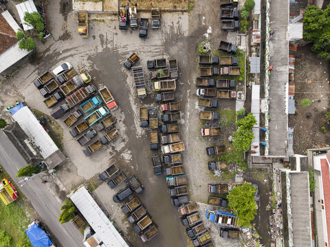Aerial view of the Animal Market Prambanan with people and rows of small trucks parked on a dirt lot in Kecamatan Prambanan, Jawa Tengah, Indonesia.