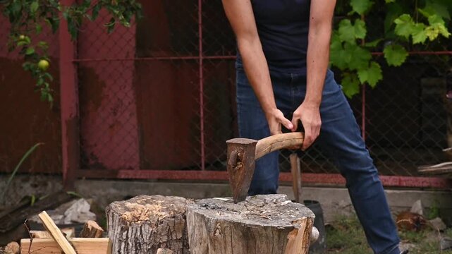 Man splitting log with heavy axe, wood flying as ax hits log. Backyard setting with chopped timber, person in dark shirt performing strong chopping action, outdoor natural lifestyle, closeup detail.