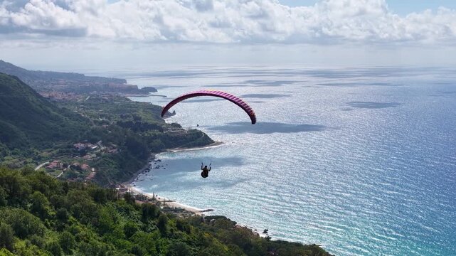 Tracking Aerial View of Paragliding Pacarhute Flying Above the sea and the coastline of Tropea, Italy. Summer Activity and Adrenaline Concept, Drone Shot