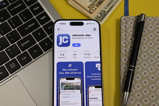 Kiel, Germany - 05-20-2026: Smartphone displaying the Jobcenter-App job search and employment services app in the App Store in a workspace environment with laptop and notebook
