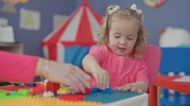 Little girl placing multicolored toy blocks with her hand on a pegboard activity table in a colorful classroom; concentration learning.
