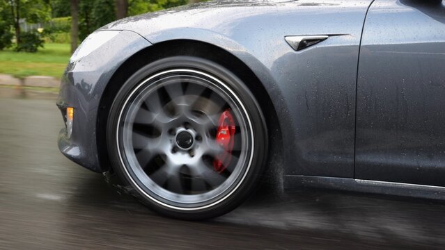 Wheel of modern electrical automobile driving at urban road on rainy day. Ecology friendly car riding moving along motorway. Electric vehicle riding through empty highway. Green innovation concept