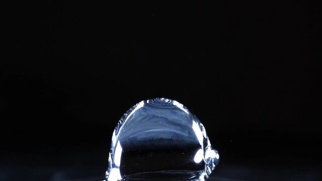 Single clear water drop falling slowly, macro liquid motion on black background