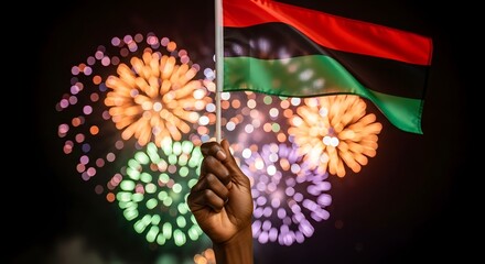 Hand holding panafrican flag against a backdrop of colorful fireworks celebrating juneteenth