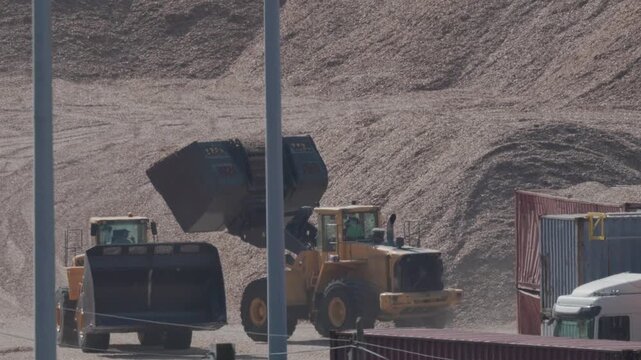 Heavy machinery moves materials in a construction site with trucks at work near a gravel pile in the afternoon