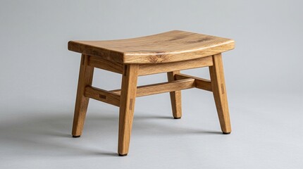 Fototapeta premium Small solid oak footstool with curved seat and tapered legs isolated on gray background featuring traditional woodworking joinery for comfortable ergonomic seating.