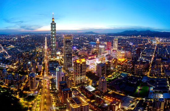 Aerial panorama of Downtown Taipei at dusk, the vibrant capital of Taiwan, with 101 Tower standing out among skyscrapers in Xinyi Commercial District and city lights dazzling under blue twilight sky