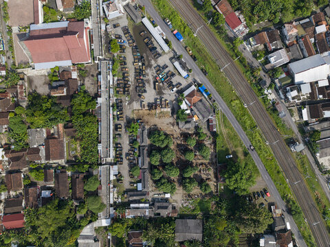 Aerial view of Animal Market Prambanan with trucks parked near stalls, lush green trees, and a railway line running alongside a road in Kecamatan Prambanan, Jawa Tengah, Indonesia.