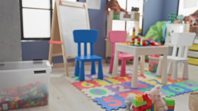 Little girl playing with toy blocks on colorful foam number mat beside small table in a building playroom; joyful play.