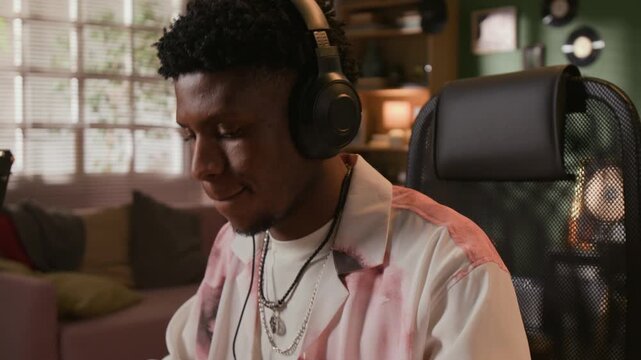 Tilt up shot of focused Black male music producer playing MIDI controller while composing new electronic sounds in home recording studio