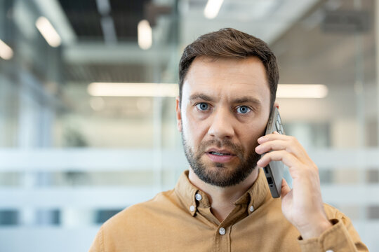 Concerned businessman on phone in office, listening intently with a serious, worried expression as he receives difficult news or handles a tense professional conversation