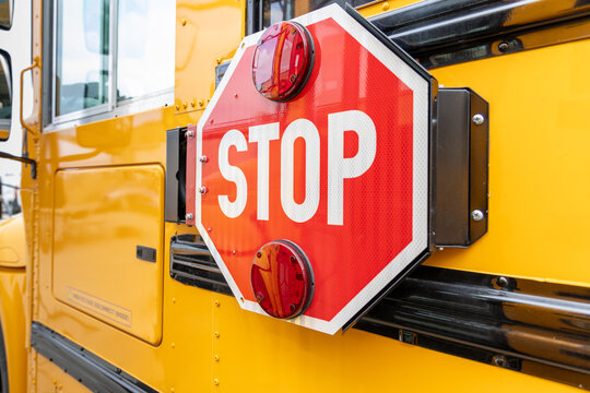 Close-up of a red stop sign attached to the side of a yellow school bus