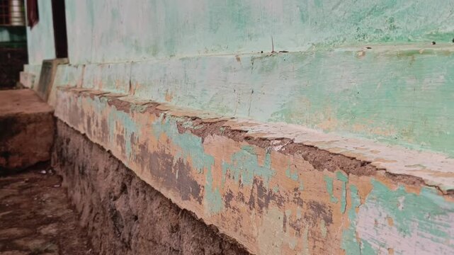 Low angle tracking footage of a damaged wall base with flaking green paint and exposed crumbling concrete.