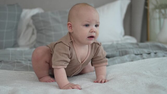 Happy baby. Cute little newborn girl with smiling face sitting on bed in bedroom. Infant baby resting playing crawling on blanket at home. Motherhood happy child childcare concept